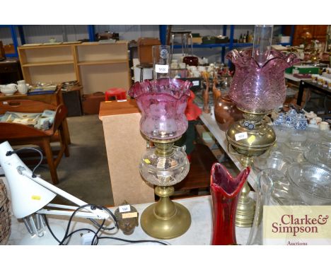 A brass oil lamp with glass reservoir and amethyst coloured shade and glass chimney