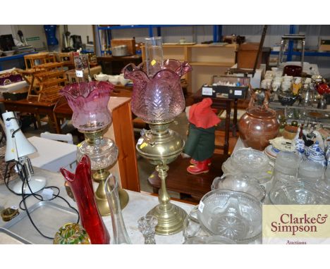 A brass oil lamp with amethyst coloured light shade and glass chimney
