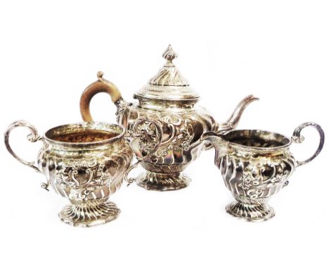 A late Victorian ornate silver three piece tea set of small form with pedestal feet and profuse embossed decoration, the teap