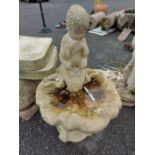 A concrete birdbath in the form of putti perched on a shell