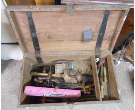 A wooden toolbox containing a quantity of old tools including braces, saws, etc.