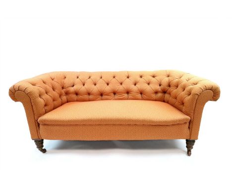 A small Edwardian upholstered chesterfield sofa, covered in a red and pale terracotta coloured material with a foliate motif 