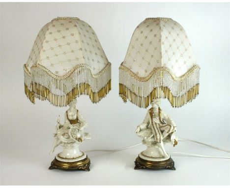 A pair of Capodimonte porcelain lamp bases circa 1970s, modelled as male and female figures seated upon a rock with gilded de