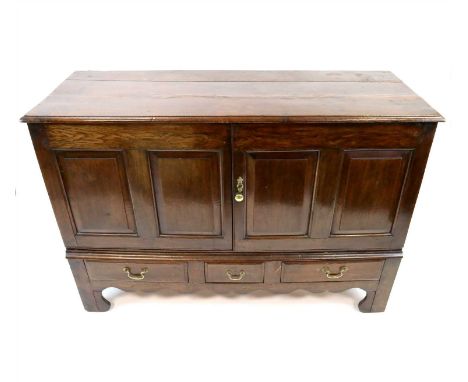 A large George III panelled oak sideboard, the bevelled plank top above a pair of twin panelled doors opening to reveal a she