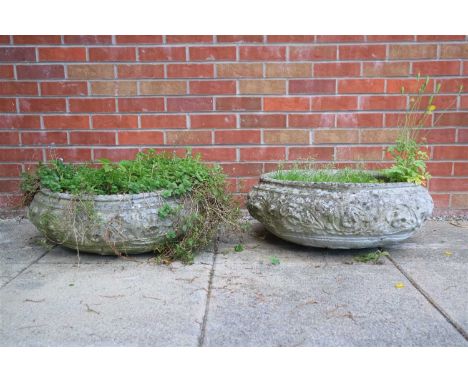A pair of weathered simulated limestone garden planters of squat bulbous form, moulded with floral and foliate motifs, raised