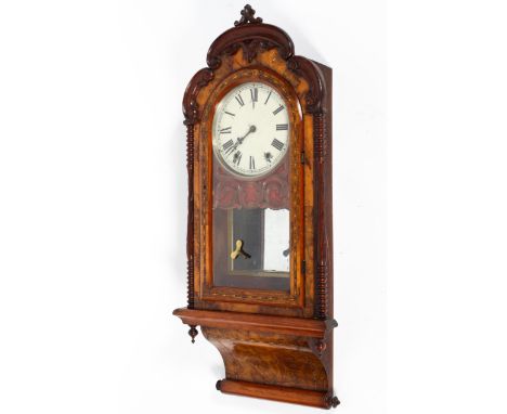 A Seth Thomas burr walnut striking wall clock, inlaid with stringing, carved with acanthus scrolls and flanked by two turned 