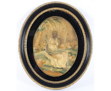 A late 18th century silk needlework picture of oval form, depicting a woman holding a bird in tropical and architectural land