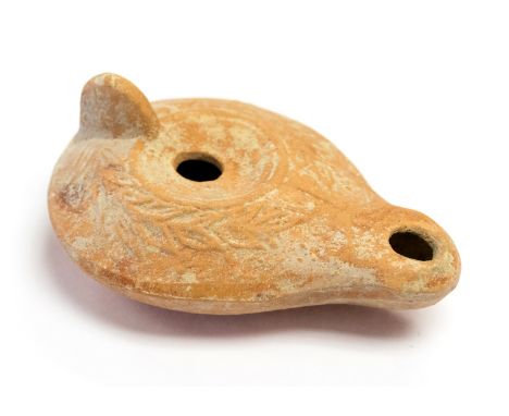 Roman pottery oil lamp of a red colour. It is 93 mm long by 69 mm wide. It is of the flatter early style and is decorated wit