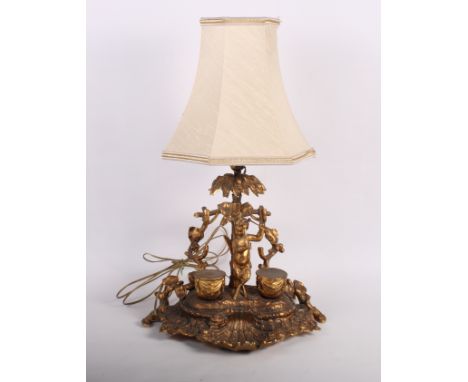 A late 19th Century gilt metal desk inkstand formed as a cherub playing two drums, 12" high (now converted as a table light)