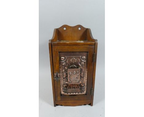 An Art Nouveau Oak Smokers Cabinet, with Hinged Door Decorated with copper embossed Flowing Foliate Stylised Panel, Enclosing