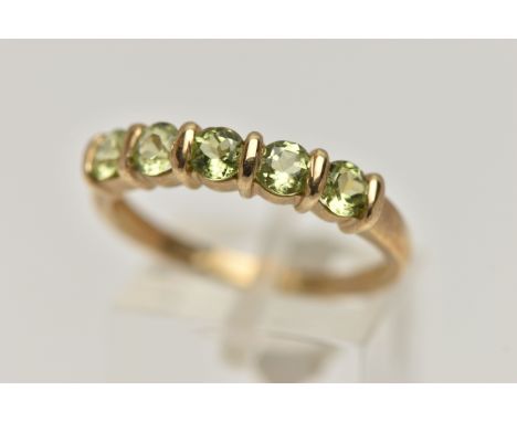 A 9CT GOLD PERIDOT RING, set with a row of five circular cut peridots, each tension set, to a polished yellow gold band, hall