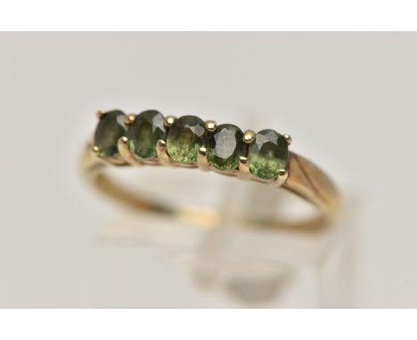 A 9CT GOLD FIVE STONE RING, set with a row of five oval cut green sapphires, each claw set to a yellow gold shank, hallmarked