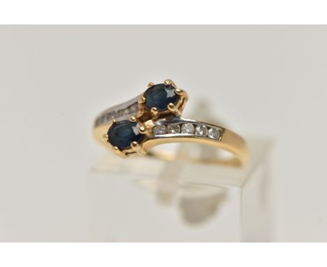 AN 18CT GOLD SAPPHIRE AND DIAMOND RING, cross over design, set with two oval cut blue sapphires, and round brilliant cut diam