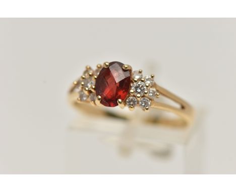 A YELLOW METAL GARNET AND DIAMOND RING, centring on an oval cut garnet four claw set, flanked with round brilliant cut diamon