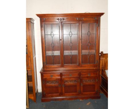 An Old Charm oak display cabinet, the outswept pediment over two glazed doors enclosing two glass shelves, over three drawers