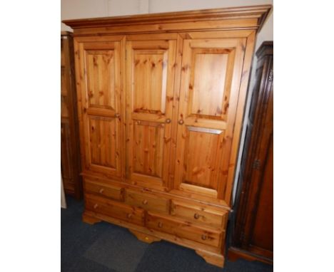 A pine triple wardrobe, the outswept pediment over three doors, above three short and two medium drawers, raised on bracket f