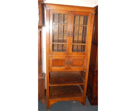 An early 20thC oak bookcase, with two glazed doors enclosing two shelves over cupboards and two open shelves, raised on brack