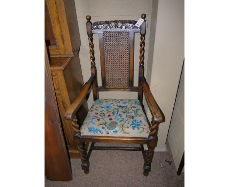 An early 20th Century carved and stained oak carver chair, with carved cresting rail of centre cane panel by spiral twist col