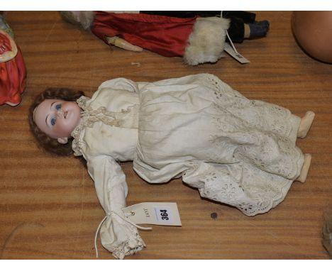 An antique German bisque head doll with brown hair, fixed blue eyes and open mouth, wearing a cream coloured lacy costume.