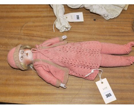 An antique German bisque head doll, with blond hair, rolling eyes, open mouth, wearing a pink knitted costume.