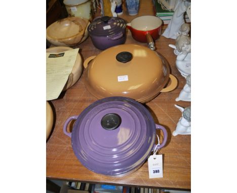 Two graduating Le Creuset casseroles and covers in plum coloured enamel; a large circular Le Creuset pan and cover; and a red