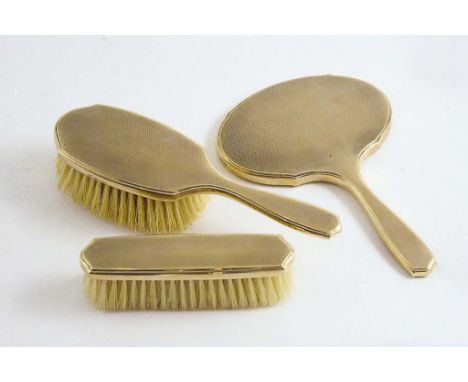 GOLD:- A 9 ct. three piece dressing table set of two brushes & hand mirror with engine turned decoration in fitted case