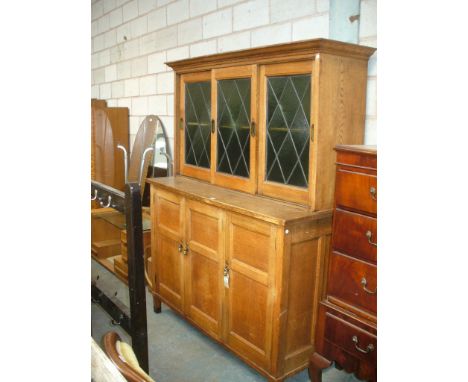 A late 19th early 20th Century oak housekeepers cupboard, with a cavetto cornice above three leaded coloured glass sliding do