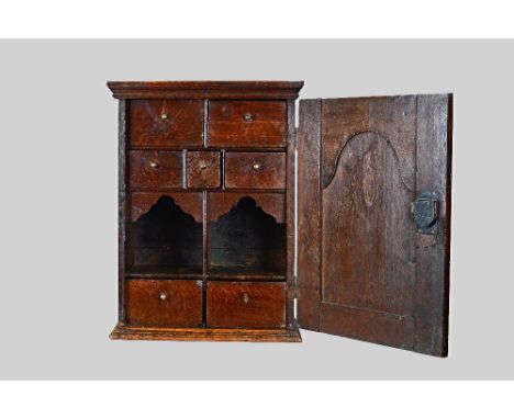 A 17th century oak spice cupboard, the arch panel door enclosing a seven drawer and twin recess interior, 47cm wide x 62cm hi