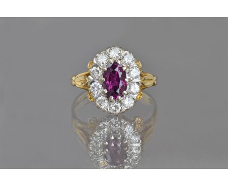 An 18ct gold, ruby and diamond oval cluster ring, claw set with the oval cut ruby to the centre in a surround of ten circular