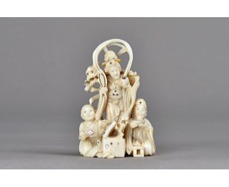 A small Japanese ivory and mother-of-pearl inlaid okimono, Meiji period, carved as Kannon standing with a dragon across her s