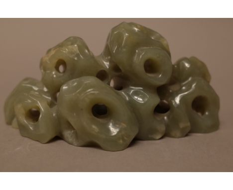 A Chinese celadon jade brush rest, carved as a group of pierced rocks, 11.5cm. wide.Provenance; From a distinguished UK schol