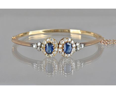 A gold, sapphire and diamond set oval hinged bangle, in a twin cluster design, each cluster claw set with a cushion shaped sa