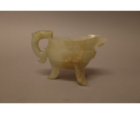 A Chinese archaistic jade libation cup, raised on three splayed supports, the sides carved with a band of taotie masks, the s