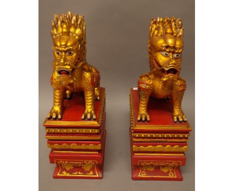 A pair of Chinese gilt and red painted stone figures of dragons, 20th century, each modelled seated on a rectangular plinth, 