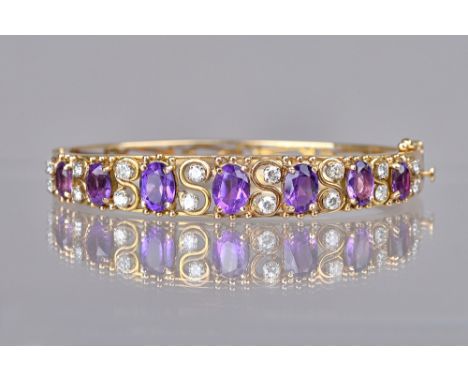 A gold, amethyst and diamond set oval hinged bangle, the front mounted with a row of seven graduated oval cut amethysts and w