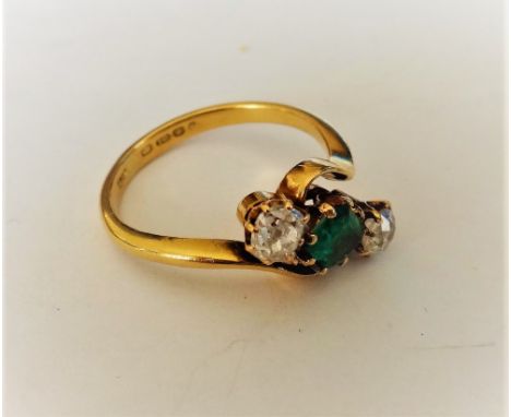 An 18ct gold, emerald and diamond three stone ring, claw set with the cut cornered rectangular step cut emerald at the centre