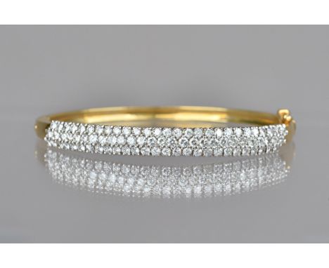 A gold and diamond set oval hinged bangle, mounted with three rows of circular cut diamonds, on a snap clasp, with a foldover