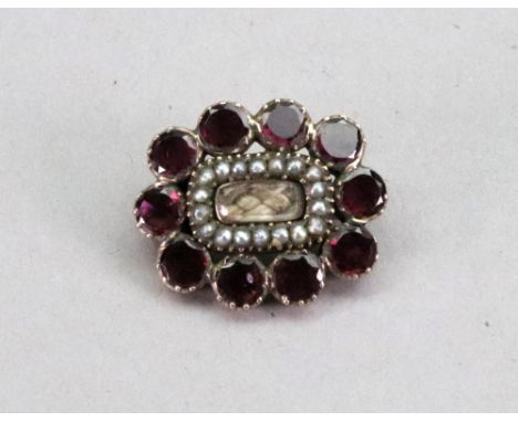 A gemset and seed pearl mourning brooch, the central hair locket compartment within a surround of seed pearls and purple gems