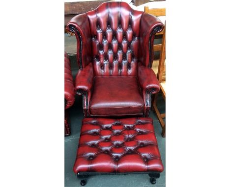 A wing back armchair, upholstered in oxblood vinyl leather, with button back, along with a matching foot stool