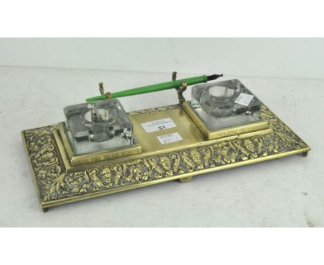 An embossed brass dual inkwell stand with pen rest, two glass inkwells, 32cm wide