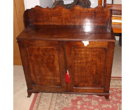An early 19th Century mahogany low cupboard with shaped scalloped back board and reeded top enclosed two panelled doors, on b