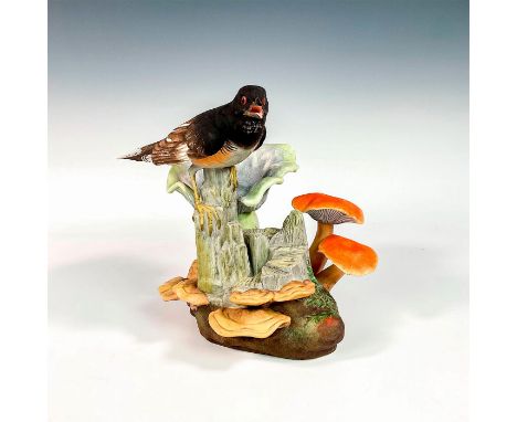 A beautiful hand crafted and hand painted bird, in a black and orange coloration, perched on a mushroom covered tree trunk. B