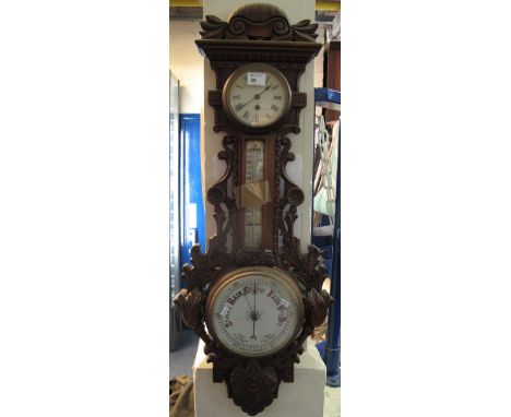 Early 20th Century carved clock barometer of wheel form with foliate and scroll moulded decoration, enamel faced, single trai