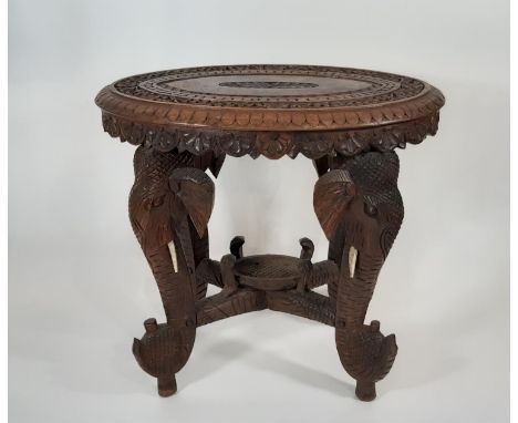 An Indian carved hardwood side table, the oval top supported on elephant head and trunk. 46cm wide x 43cm high 