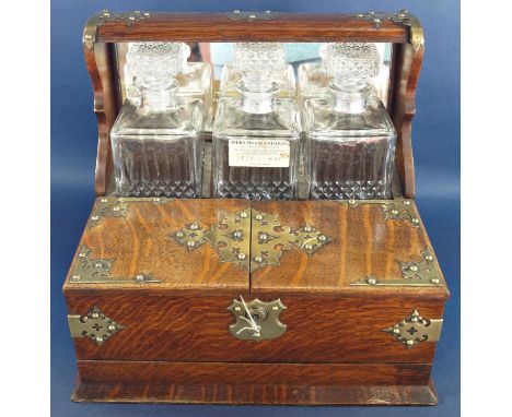 A Victorian oak games tantalus with brass overlay, having three matching decanters and two glasses, with a secret drawer to b