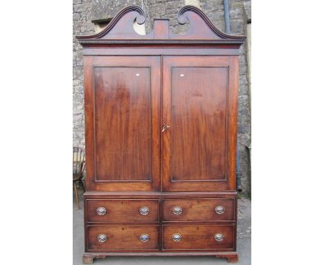 A George III mahogany linen press with broken swan neck architectural pediment, over a pair of rectangular panelled doors, en
