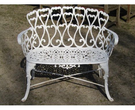 Small decorative cream painted cast iron garden bench with pierced scrolling foliate detail and swept supports united by an X