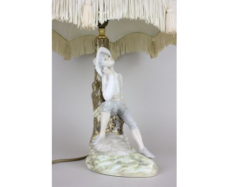A Spanish porcelain figural lamp base of a young boy seated by a tree, 36cm high