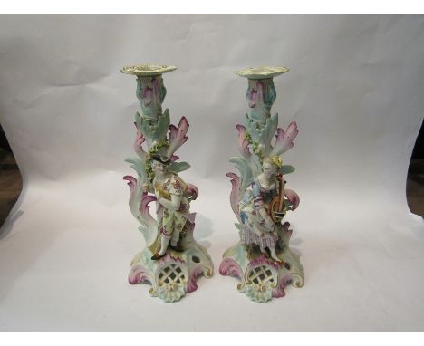 A pair of ceramic candlesticks (converted to lamp holders) depicting a man and woman in classical setting, crossed sword mark