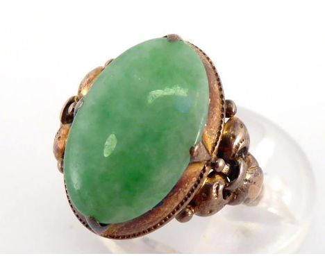 A jade ring, the oval cabochon stone 15.4 x 9.8mm, to fleur de lys shoulders, the shank stamped '14k', finger size J, 3.2gms 